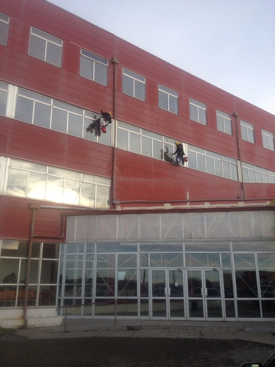 Operarios suspendidos sobre fachada roja durante trabajo en altura