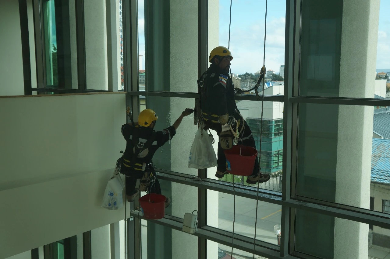 Dos operarios de Vertical Magallanes trabajando suspendidos frente a cristales